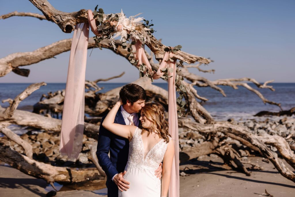 Bride and Groom embrace beside Jekyll Island Driftwood.