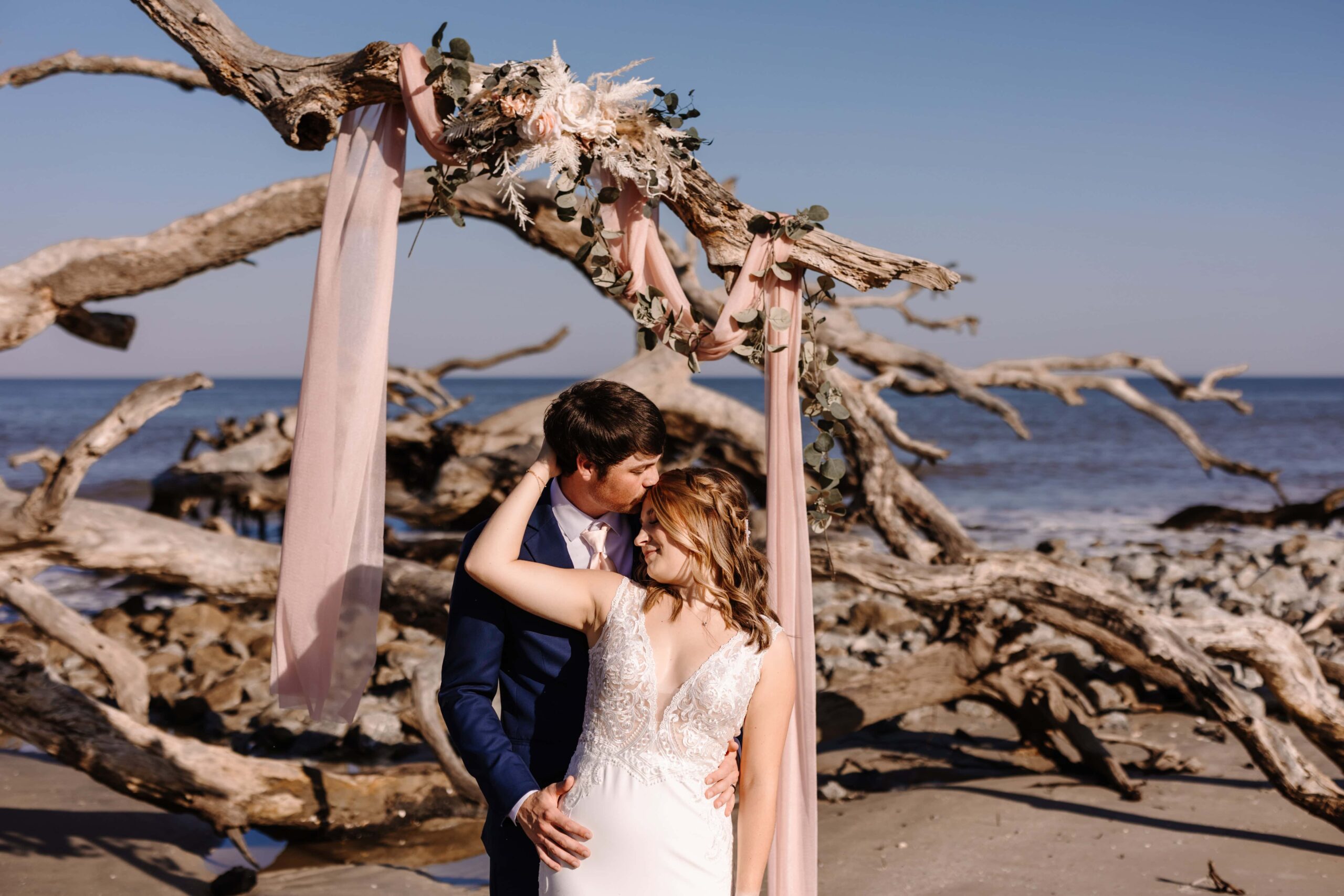 Bride and Groom embrace beside Jekyll Island Driftwood.