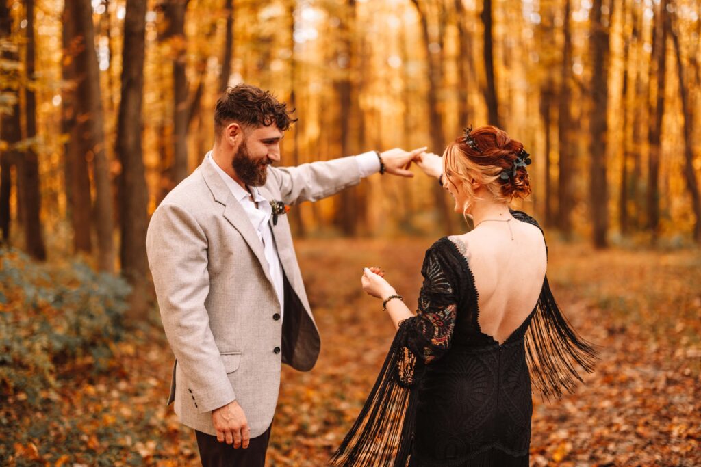 Groom spins bride in a black dress in a beautiful Autumn forest. 
