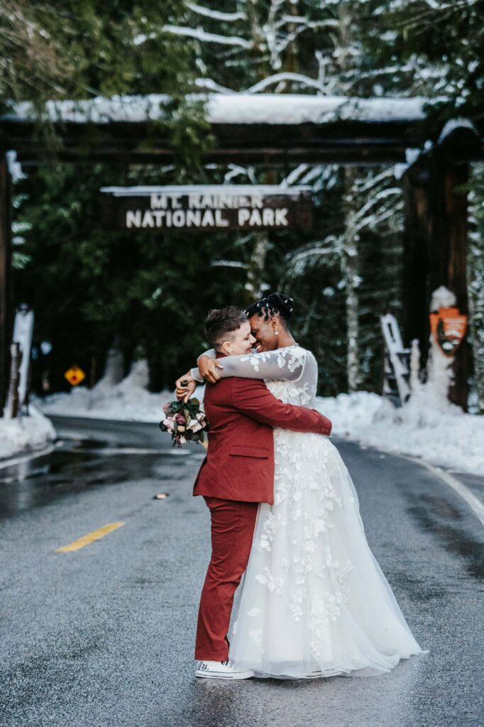 Gorgeous brides embrace beneath the Mount Rainier National Park sign.