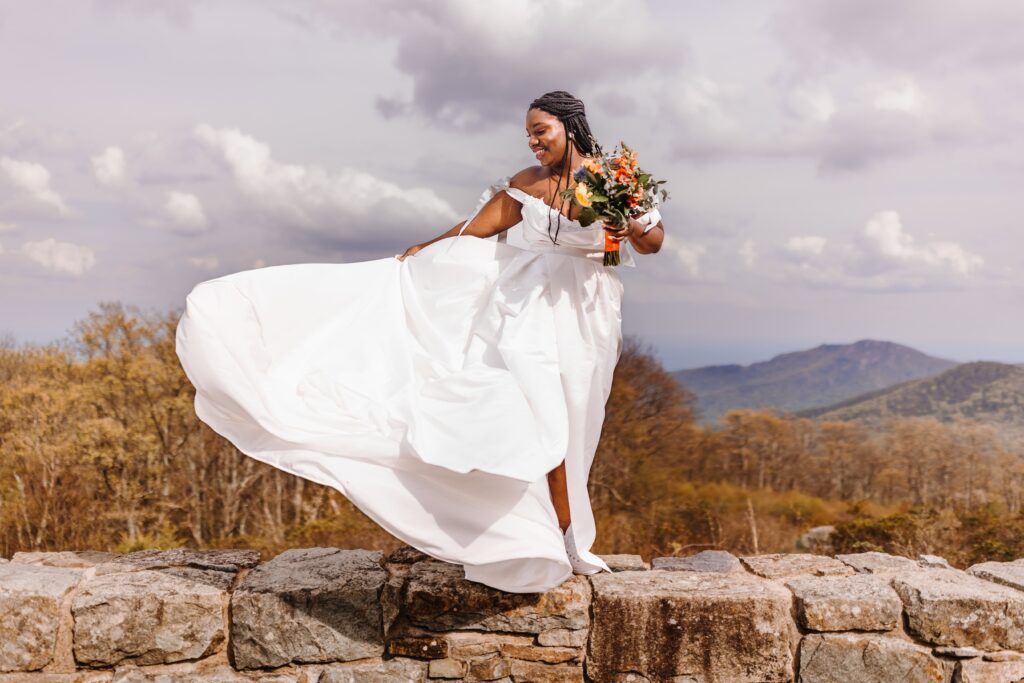 A gorgeous bride stands atop the rocks with her bouquet, dress blowing in the wind near Luray Caverns.