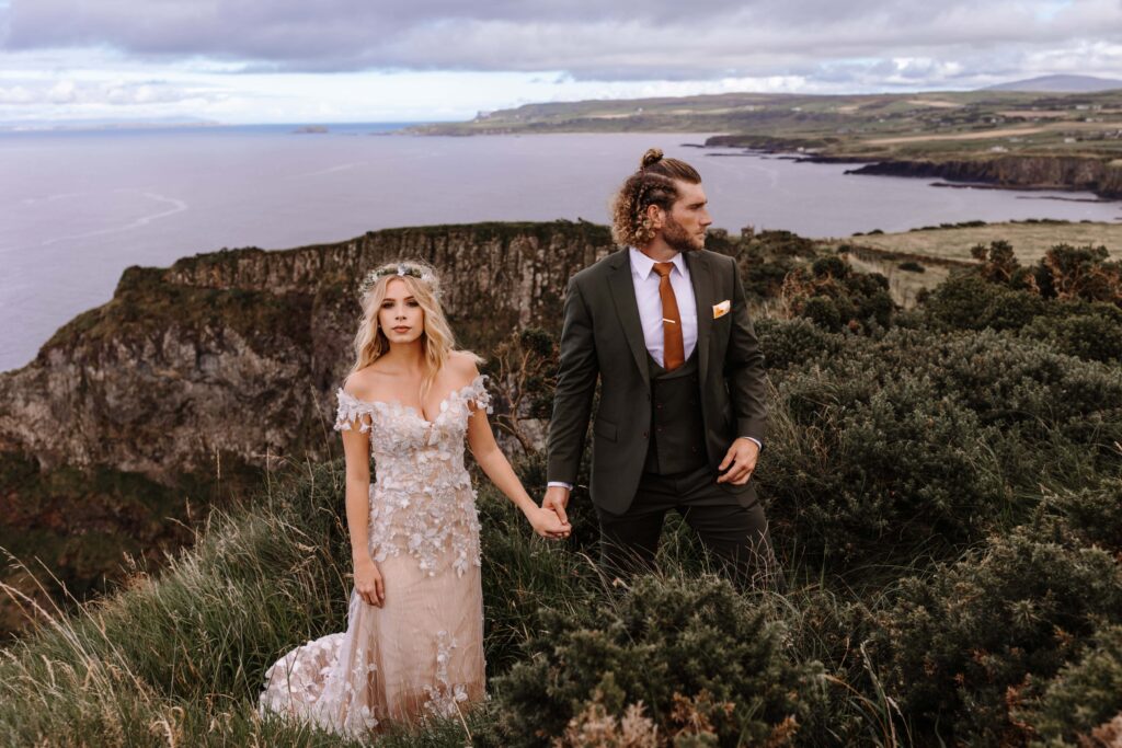 Newlyweds take a stunning portrait atop a cliffside in Northern Ireland during their destination elopement in Northern Ireland during their adventure elopement abroad.