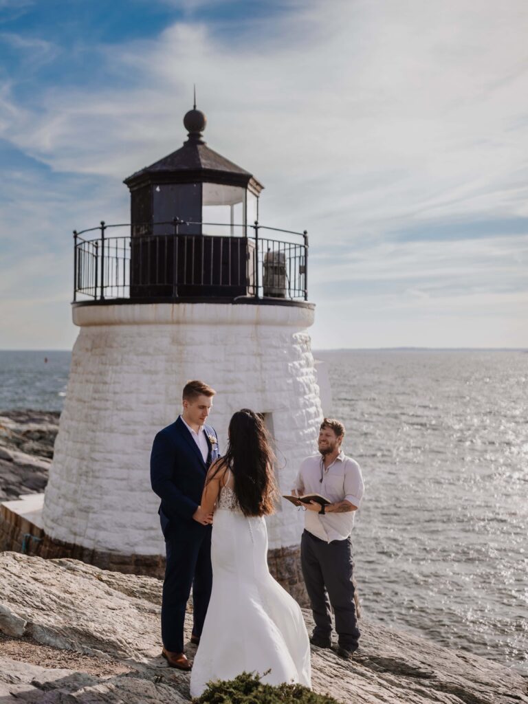 A couple and officiant standing before a seaside lighthouse wedding location
