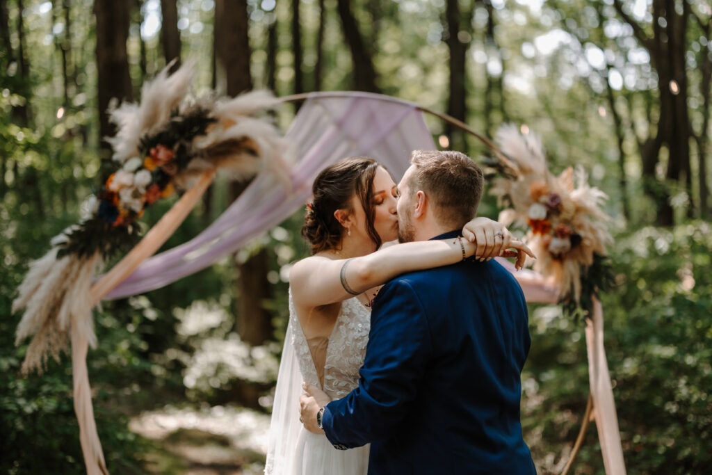 Couple shares their first kiss at the altar in front of an arch with vibrant colors.