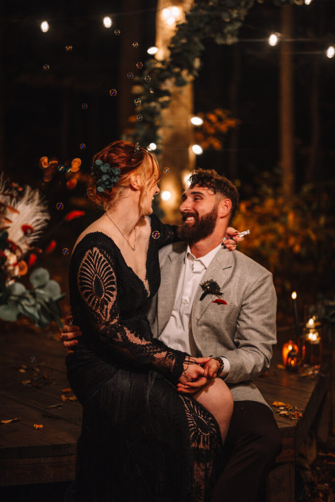 Couple laugh under the light of the beautifully lit forest platform.